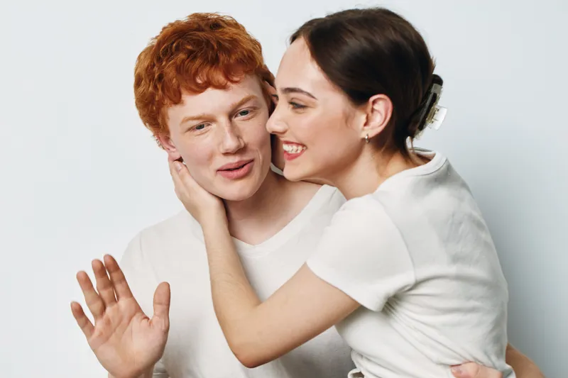 Couple, woman and man hugging and smiling with love, affection and happiness. Young people in casual clothes with joyful emotion on white background in studio.