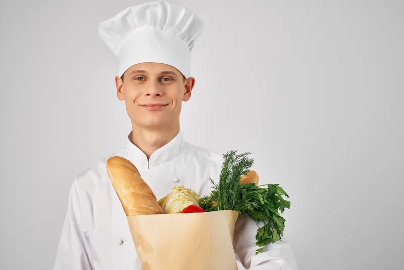 Мужчина в одежде повара держит пакет с продуктами, готовит еду на кухне