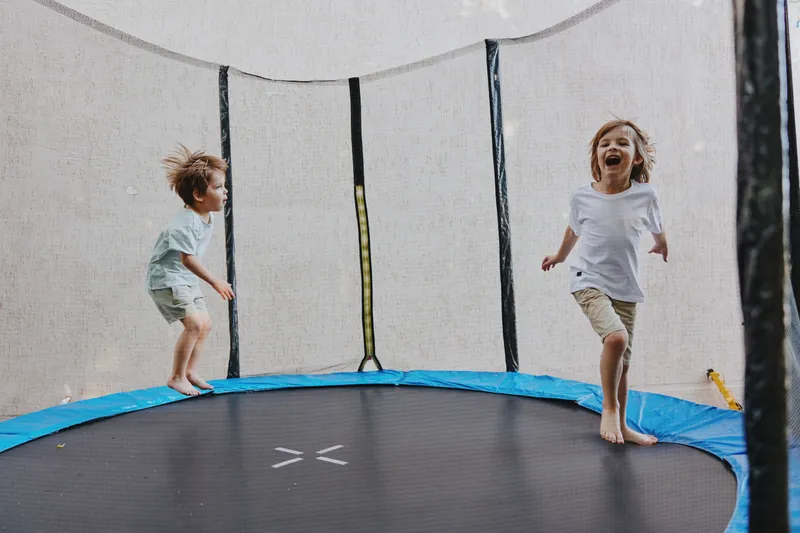 Happy children jumping on a trampoline in a joyful outdoor setting, showcasing fun, playfulness, and excitement in a sunny atmosphere.
