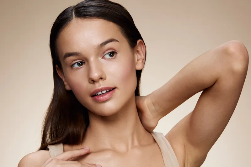Young woman with healthy skin and natural makeup, expressing confidence and beauty against a neutral background Perfect for skincare and wellness concepts