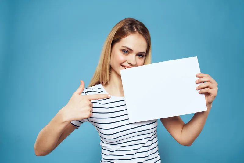 Эмоциональная женщина держит в руках лист бумаги, крупный план, стиль жизни, синий фон, место для копирования
