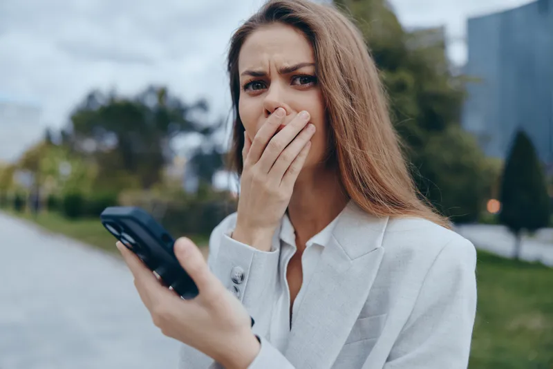 upset woman holding phone with worried expression in outdoor urban setting conveying financial crisis and stock market fall emotions