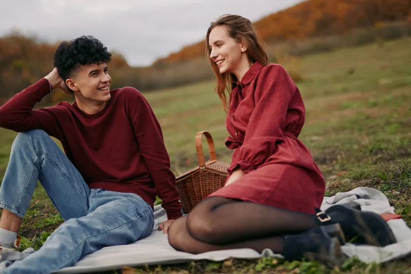 A candid outdoor scene of a young couple on a picnic, focused on genuine smiles and warm body language that emphasize natural connection, authenticity and subtle credibility in the moment.