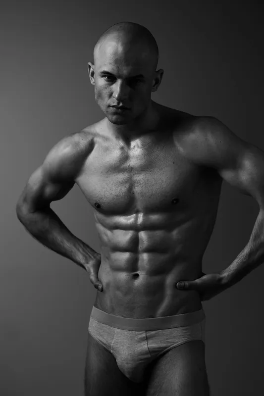 Black and white image of a muscular man posing confidently, showcasing his toned physique and strong presence, perfect for fitness and health themes.