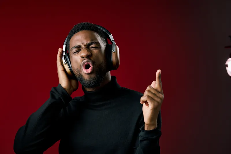 Young Black man enjoying music with headphones, expressing emotion and joy against a red background, showcasing a vibrant and energetic concept