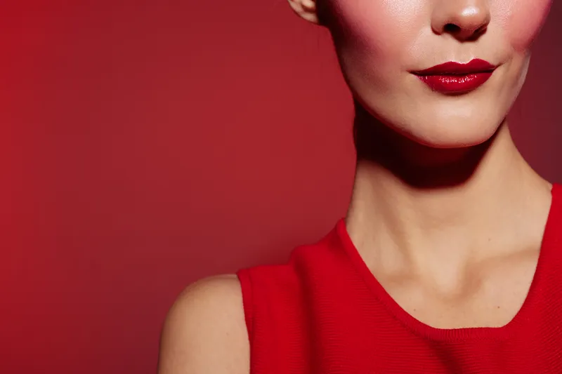 Close-up of a woman with red lipstick and red dress against a red background. Concept of beauty, fashion, makeup, and elegance with vibrant color contrast and style.