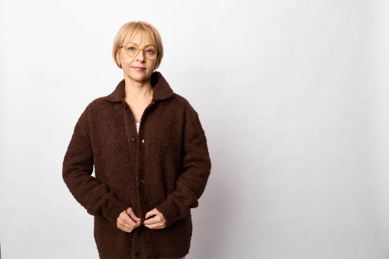 Woman senior portrait studio white coat fleece hands calm fashion, standing on clean white background, relaxed expression, warm winter outerwear, soft studio lighting