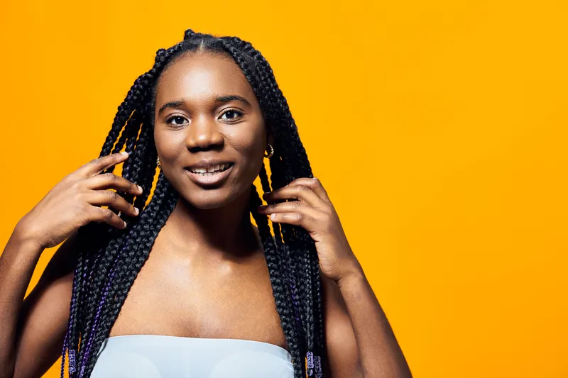 Young black woman with long braids smiling against a vibrant yellow background, showcasing confidence and beauty through natural hair styling and joyful expression