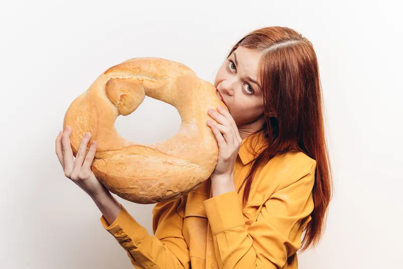 Мучное изделие, батон, и женщина в желтой рубашке на заднем плане, светлый фон, обрезанный вид