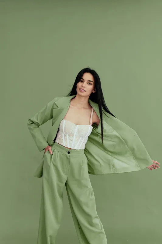 Young woman in stylish light green suit with white lace top poses confidently against a matching green background showcasing modern fashion and grace.