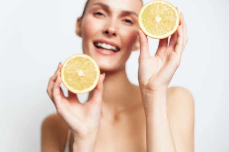 Smiling woman holding lemon halves near her face, close up on white background, skincare concept for wellness and self care, fresh citrus, soft studio lighting, healthy glow, happy mood