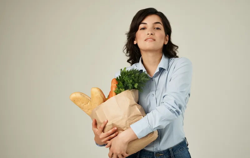 Веселая симпатичная женщина в рубашке с пакетом продуктов