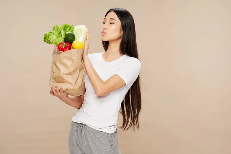 Женщина с пакетом продуктов здорового питания, овощами, стройной фигурой на бежевом фоне