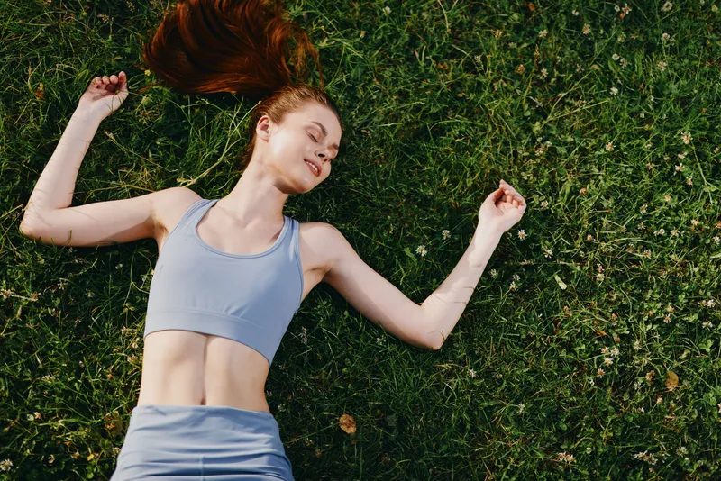 Young woman enjoying relaxation on green grass, wearing light blue sportswear, conveying peace and wellness, perfect for fitness and healthy lifestyle concepts