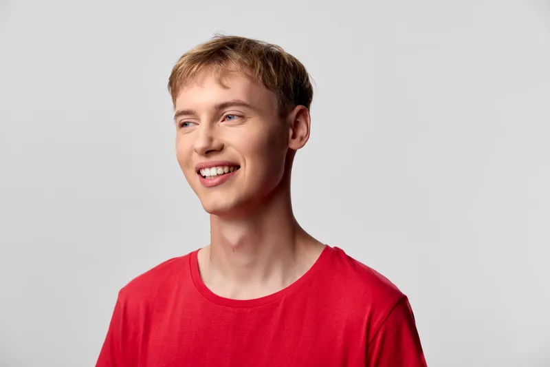 Smiling man, young adult, red shirt, casual style, studio lighting, happy expression, relaxed pose, confident look, approachable mood, warm tone, clear skin, simple background, lifestyle shot,