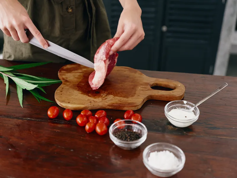 Женщина с ножом в руке нарезает свежее мясо для стейка, которое будет запекаться на кухне