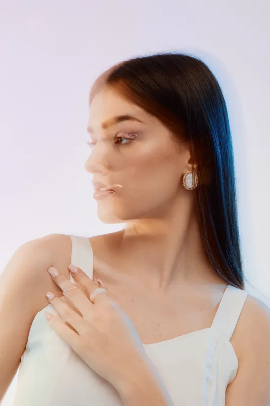 Portrait of a young woman with long hair wearing white top and earrings. Blurred double exposure effect creates artistic beauty and fashion concept in soft studio lighting.