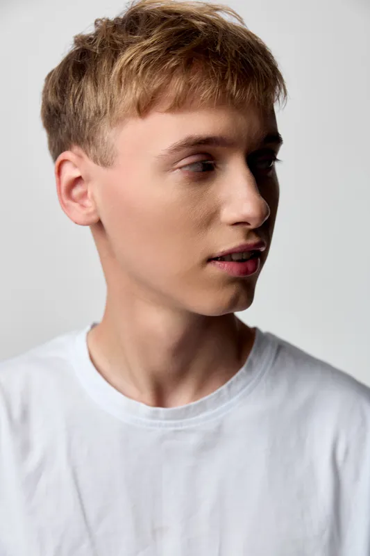 Profile view of a young man in a white t shirt, neutral studio backdrop, calm expression and soft lighting, clean minimalist style, casual fashion, modern mood, everyday elegance and focus on facial