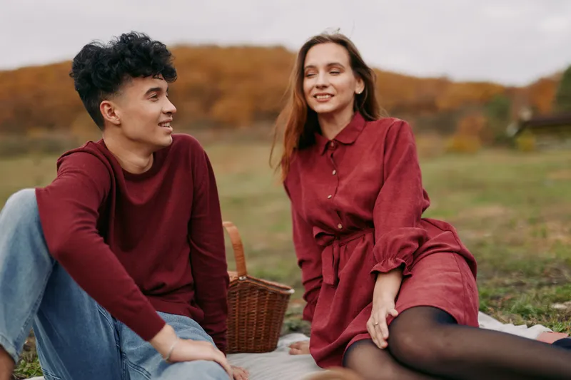 Young couple enjoying a candid autumn picnic on a blanket, sharing genuine smiles and relaxed conversation that convey authenticity and credibility in a natural lifestyle scene.