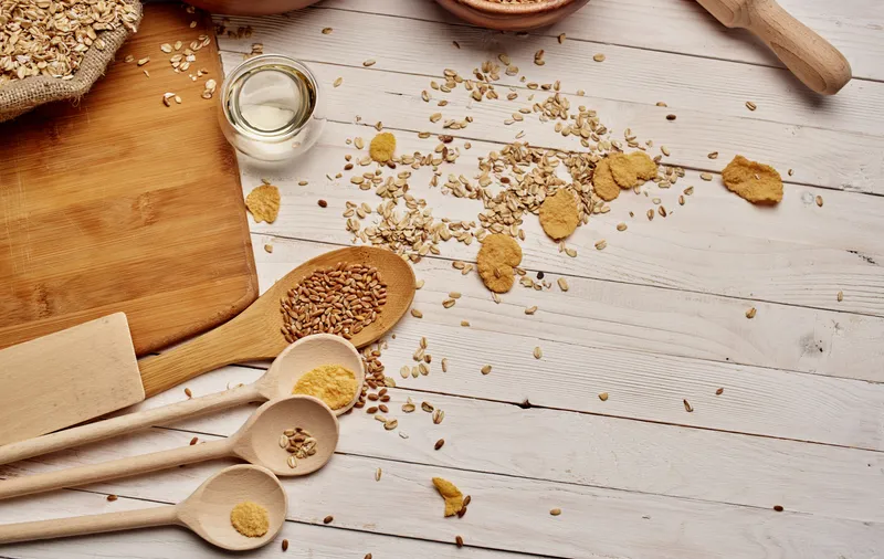 Пшеница и злаки, рассыпанные на столе, деревянные ложки, кухонная доска