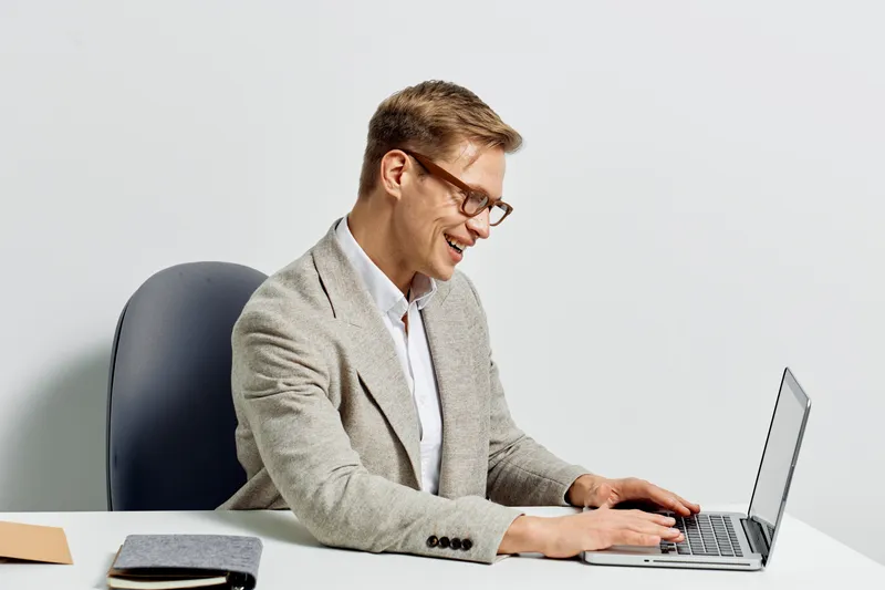 Young smiling caucasian man wearing glasses light suit typing on laptop digital nomad cyber security concept isolated on white background studio portrait