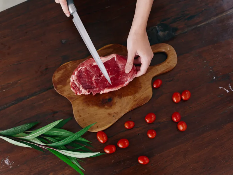 Женщина с ножом в руке нарезает свежее стейковое мясо для жарки на кухне