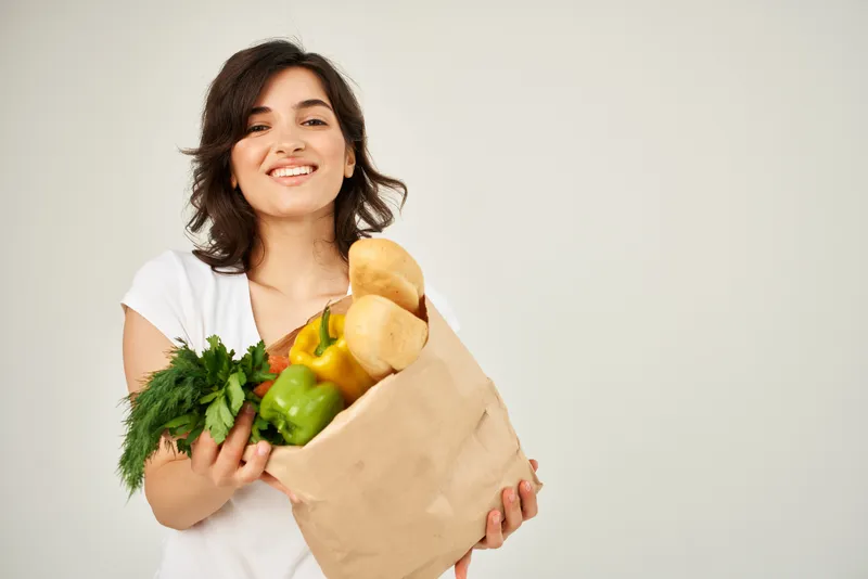 Весёлая брюнетка с продуктами и овощами на светлом фоне