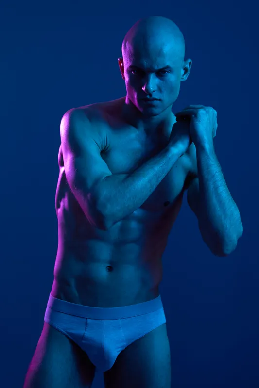 Athletic man posing in dramatic blue lighting, showcasing strong physique and confident expression. Captivating atmosphere enhances overall visual impact.