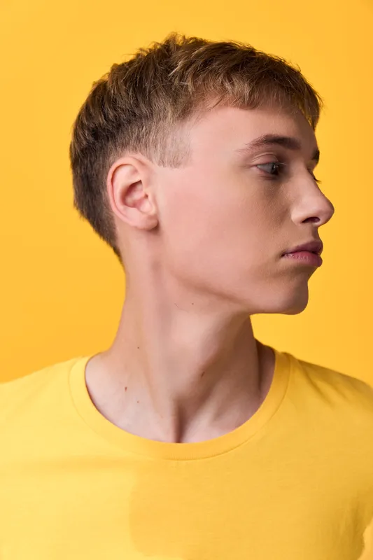 Man profile in a yellow shirt, side view against a yellow background, showcasing clean lines, calm expression, modern fashion aesthetic, versatile stock image