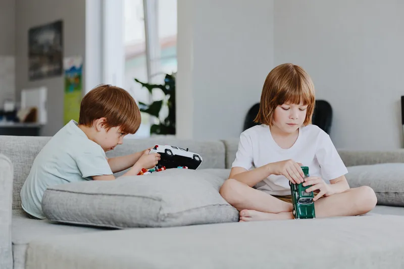 Two boys playing with toys on a sofa in a bright living room, creating a joyful atmosphere filled with fun and creativity.