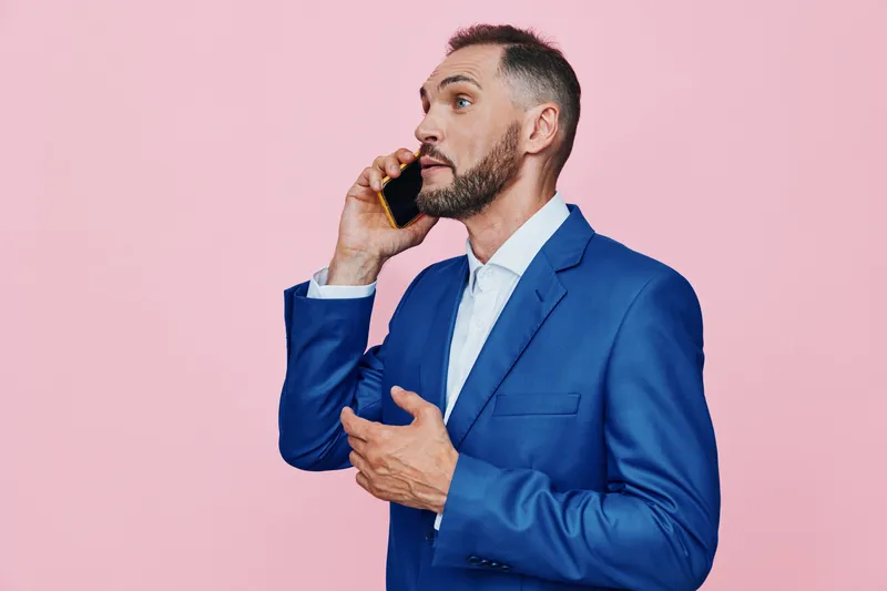 A business professional man on an isolated pink color background, speaking on a mobile phone with a confident, focused emotion and poised posture.