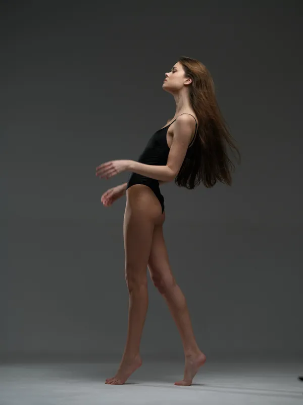 slender woman in black bodysuit posing gracefully in studio with neutral background and soft lighting