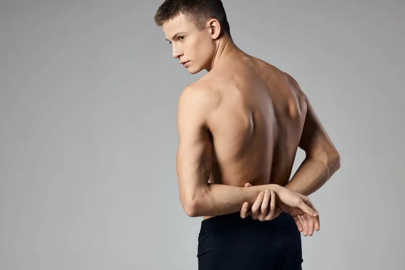 Мужчина с накачанными мышцами держит руки за спиной на сером фоне