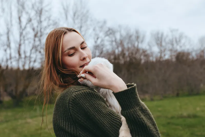 Lifestyle outdoor woman animal goat kid in field nature countryside, portrait candid happiness friendship tenderness connection breeze sunlight warmth colors green grass meadow pasture rustic scene