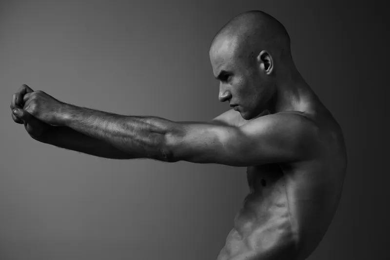 Strong man in dynamic pose showcasing powerful muscles with dramatic lighting, emphasizing strength and intensity in this black and white image.
