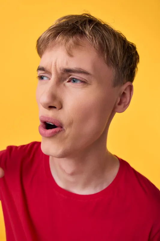 Surprised man in a red shirt speaks with wide eyes against a bright yellow backdrop, conveying emotion, energy, and spontaneous reaction for expressive, humorous, and dynamic stock photography.