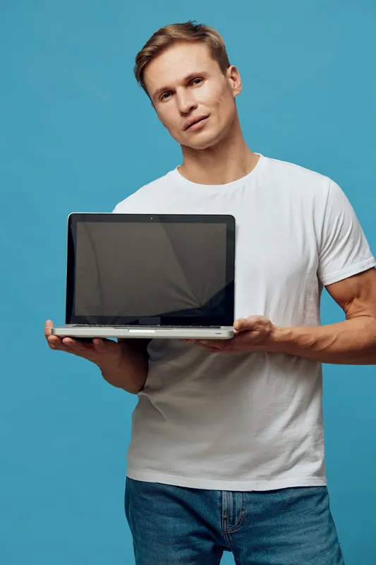 young man with laptop holding computer in hands wearing white t-shirt and jeans isolated on blue background digital nomad concept technology remote work