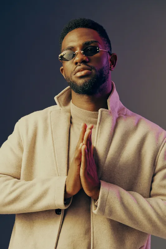 Stylish African man wearing sunglasses and a beige coat, posing confidently against a colorful gradient background, representing modern fashion and self expression