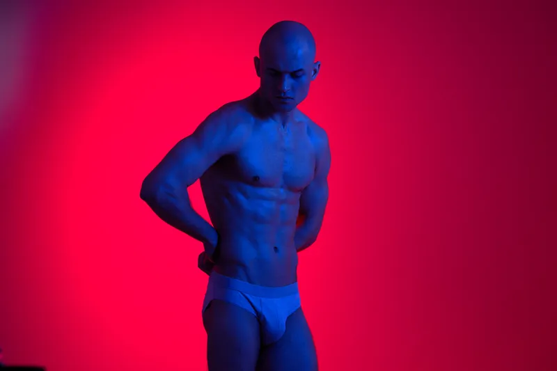 Striking male model poses in dramatic lighting, showcasing strength and confidence in a stylized setup. The image emphasizes blue and red hues for a modern appeal.