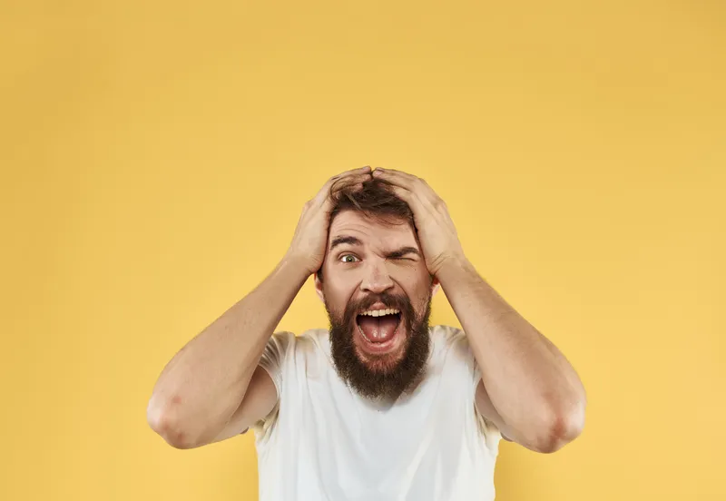 Расстроенный мужчина держит руки возле лица на жёлтом фоне