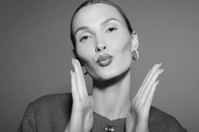 Young Caucasian woman with pale skin and slicked back hair blows a kiss with hands near face in black and white close-up portrait concept for beauty and emotion.
