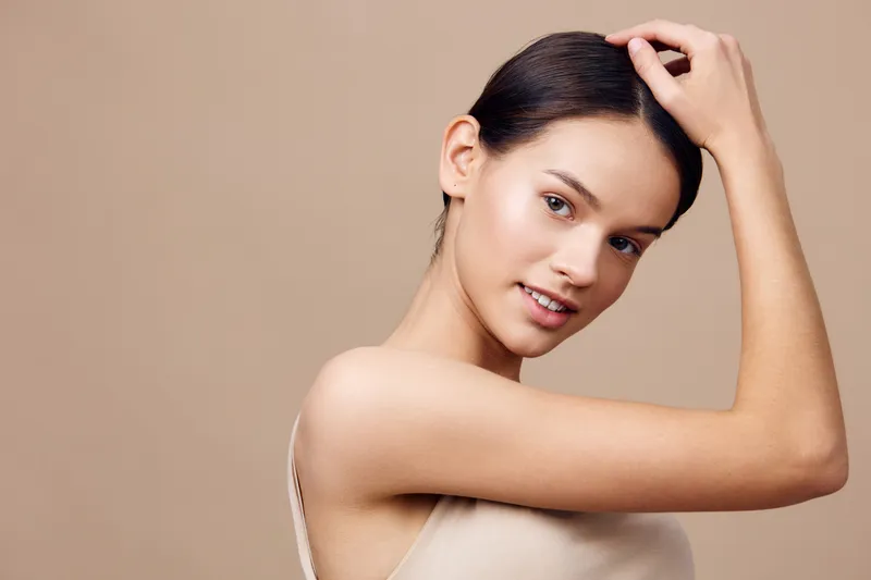 Beautiful young woman adjusting her hair against a neutral beige background, showcasing natural beauty and skin care Perfect for health and wellness concepts