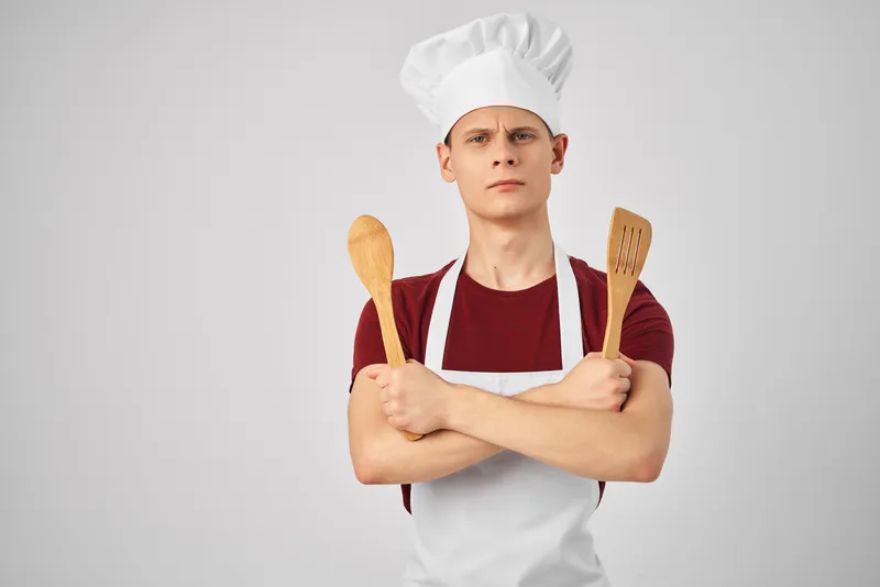 Мужчина в белом фартуке работает с кухонной утварью, занимаясь приготовлением пищи
