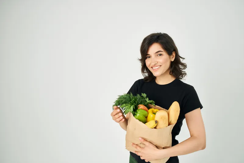 Симпатичная женщина с пакетом продуктов, здоровое питание, овощи, светлый фон
