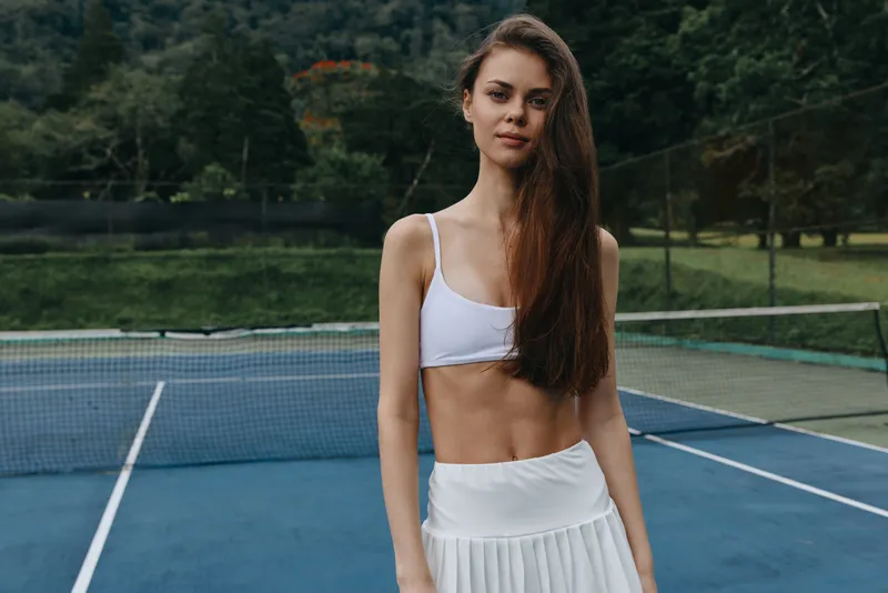 Athletic young woman in sporty attire poses confidently on a tennis court during a sunny day, showcasing a healthy lifestyle and dedication to fitness