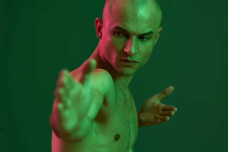 Athletic man posing with a strong expression, showcasing a dynamic silhouette against a green backdrop. The image captures strength and determination in a visually striking manner.