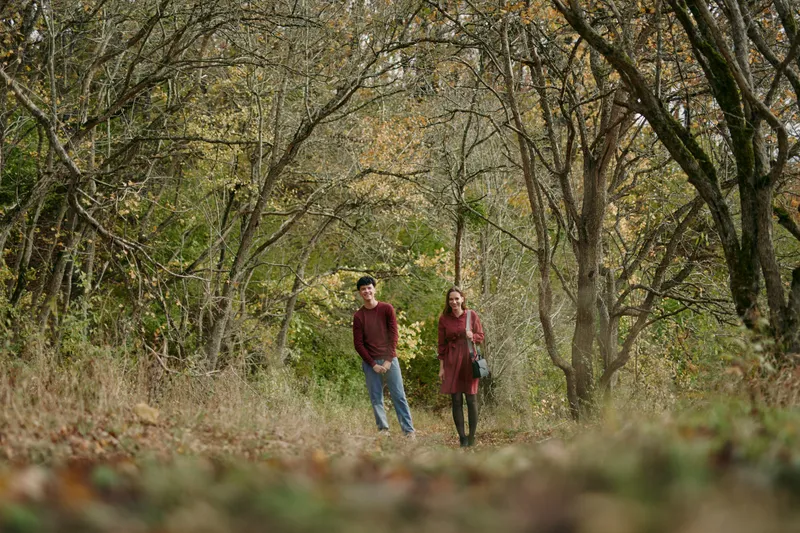 Two walkers stroll along a sunlit forest path, capturing a candid moment that feels real and authentic through natural light, relaxed posture, subtle movement, and a quiet, believable mood of