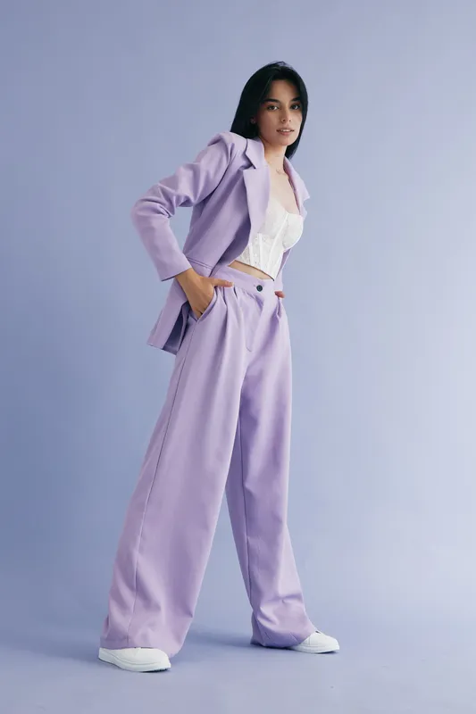 woman in lavender suit standing confidently with hands in pockets, wearing white lace top and sneakers, showcasing modern fashion and casual elegance