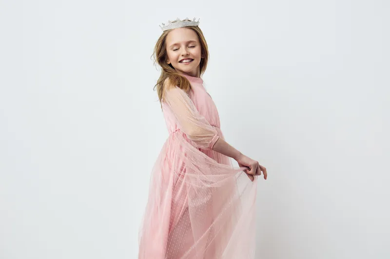 Joyful girl in a pink princess dress with a crown, expressing happiness and playfulness in a light studio setting Perfect for children s fashion and fairytale themes