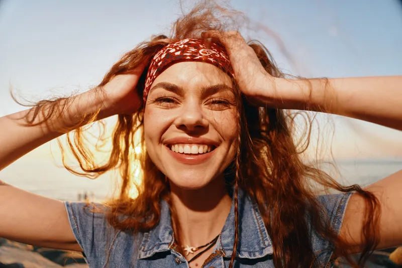 Lifestyle woman in modern boho-western denim street style with film color effect smiling joyfully under warm sunlight outdoors.